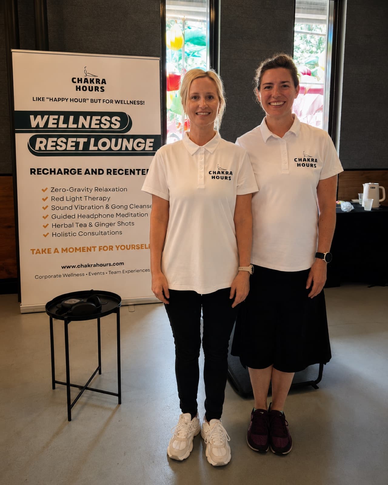Two Chakra Hours facilitators in branded polos beside the Wellness Reset Lounge banner at a Dallas corporate event, Chakra Hours