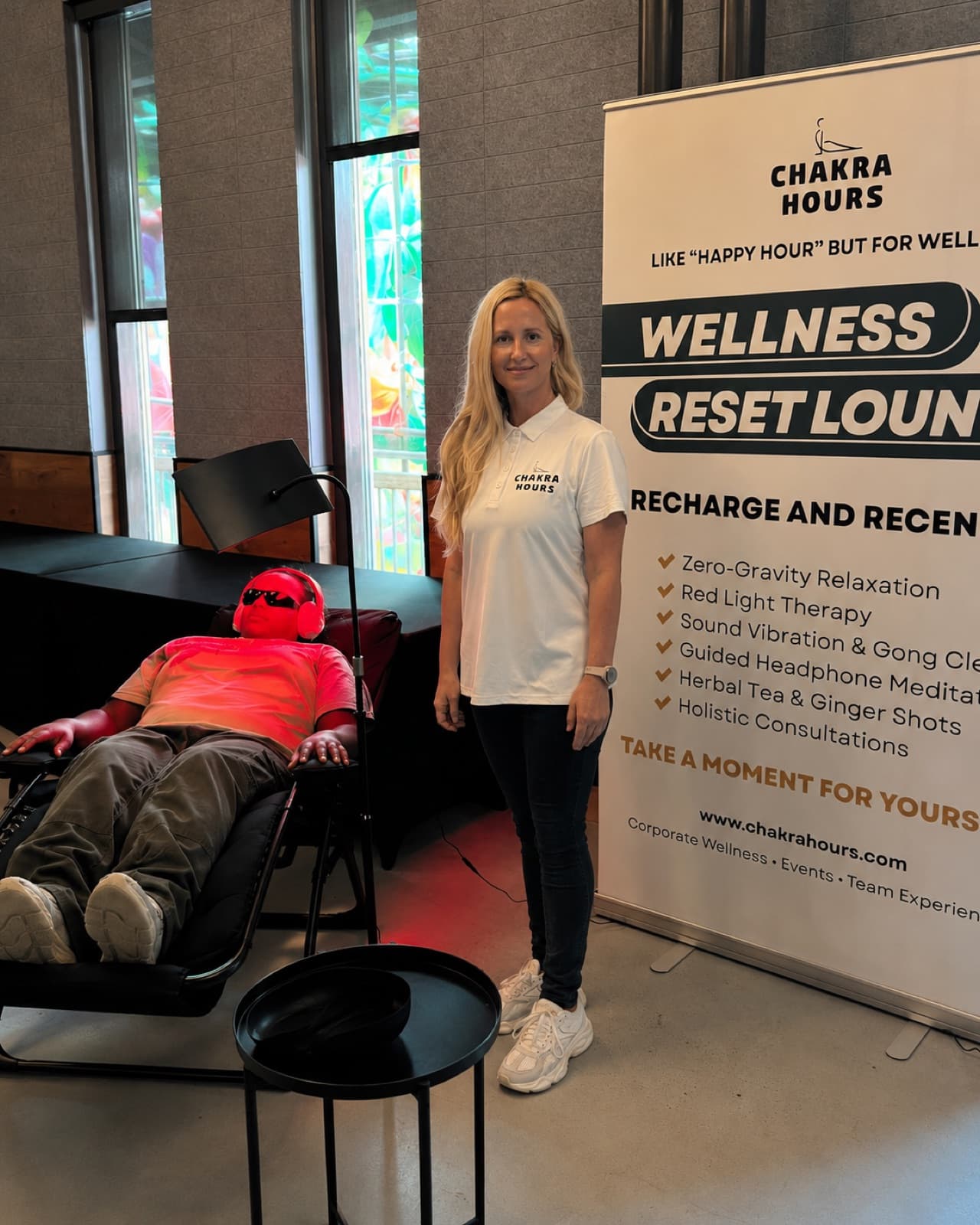 A guest relaxing under a warm red-light experience beside the Wellness Reset Lounge banner at a Dallas corporate event, Chakra Hours