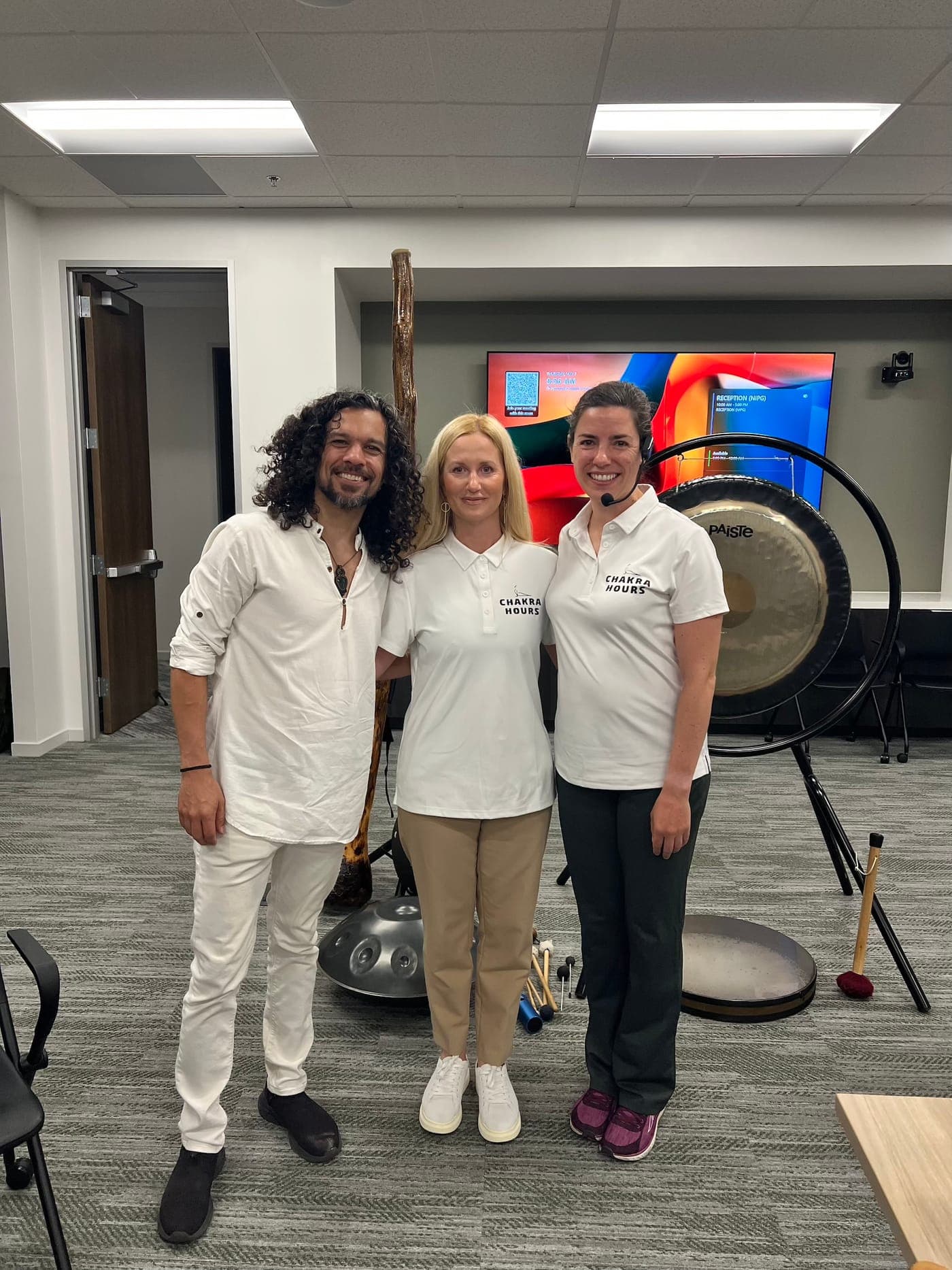 The Chakra Hours facilitator team with a gong, crystal singing bowls, and a handpan set up for a live corporate sound bath in a Dallas office, Chakra Hours