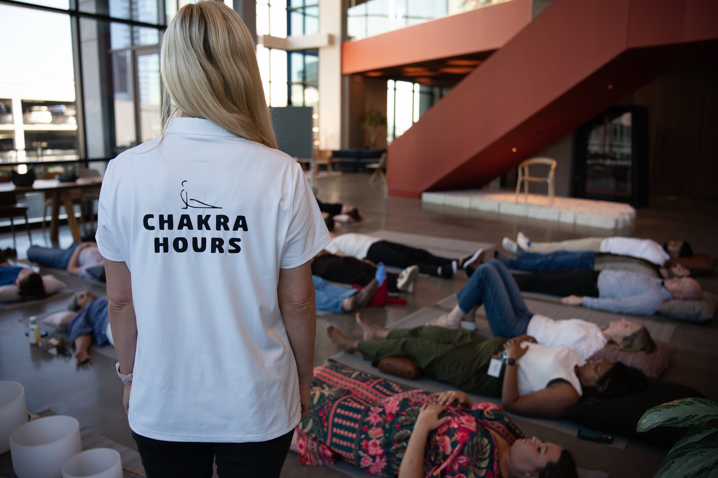 Chakra Hours facilitator in the branded polo watching over employees resting on mats at an onsite corporate wellness event in Dallas
